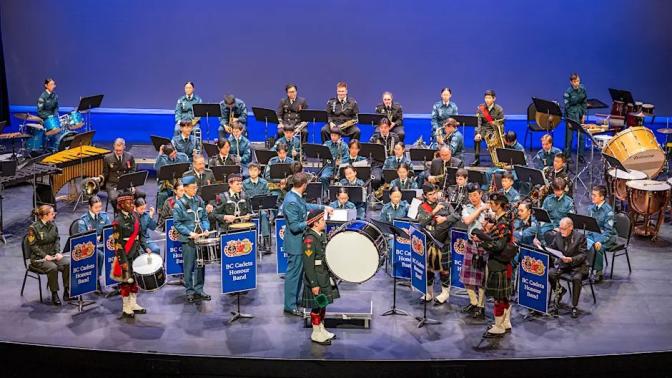 seated orchestra of musicians that are all cadets in their cadet uniforms with various instruments