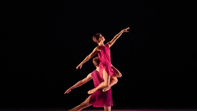 a pair of ballet dancers in dramatically lit stage performance wearing flowing crimson costumes