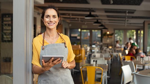 A restaurant staff member holds an ipad with chairs and tables in the background