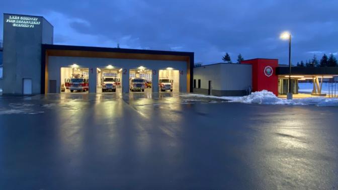 A wide shot of a fire hall taken at night, with four bay windows open and showing the fire engines ready to depart if called out.