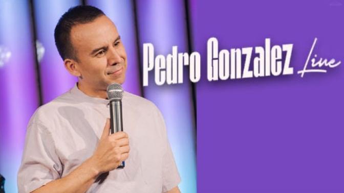 portrait of colombian comic pedro gonzalez on stage holding a microphone, He is wearing a beige tshirt, with a smile on his face and his head tilted to the left. He is standing in front of a pastel purple and light blue backdrop