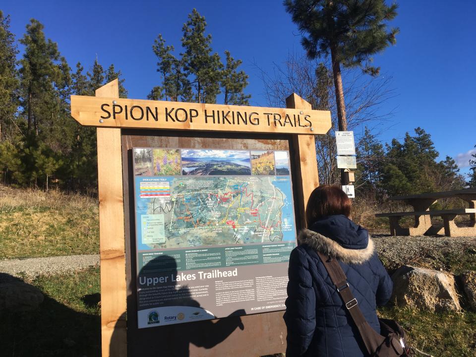 Woman reading a map at the Spion Kop Hiking Trails trailhead under a clear blue sky.