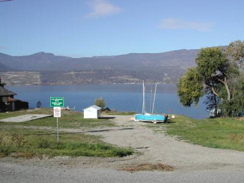 Boat launch area with a small blue and white boat, a green sign, and a view of the lake and mountains in the background.