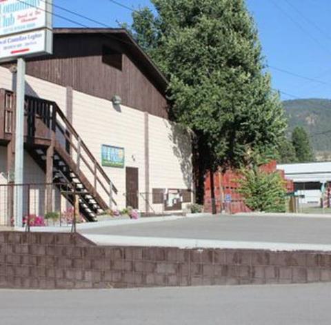 Community club building with a sign, staircase, and trees in the background under a clear sky.