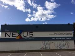 The Nexus Lake Country building with colorful logo, address, and blue sky with clouds in the background.