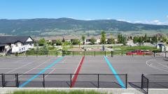 Recreational area with tennis courts in the foreground, a playground, houses, and mountains in the background under a clear blue sky.