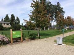 Apex Park sign with green grass, trees, and houses in the background on a clear day.