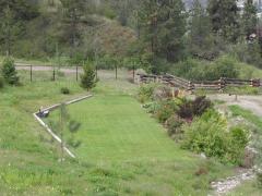 Small grassy area surrounded by wildflowers, trees, and a wooden fence in a park setting.