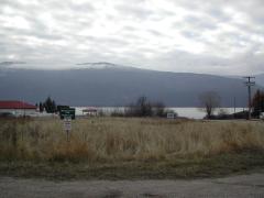 Grassy field with signs for Whiskey Cove Park Public Lake Access and a cloudy lake with mountains in the background.