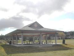 Large picnic pavilion with multiple tables under a cloudy sky in a grassy field.