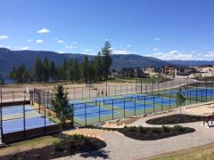 Multiple blue and green tennis courts with mountain and lake views in the background.