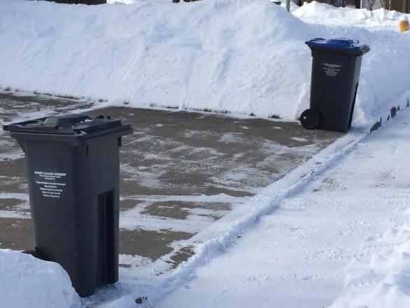 garbage and recycling carts placed on either side of a driveway in the snow for easy collection